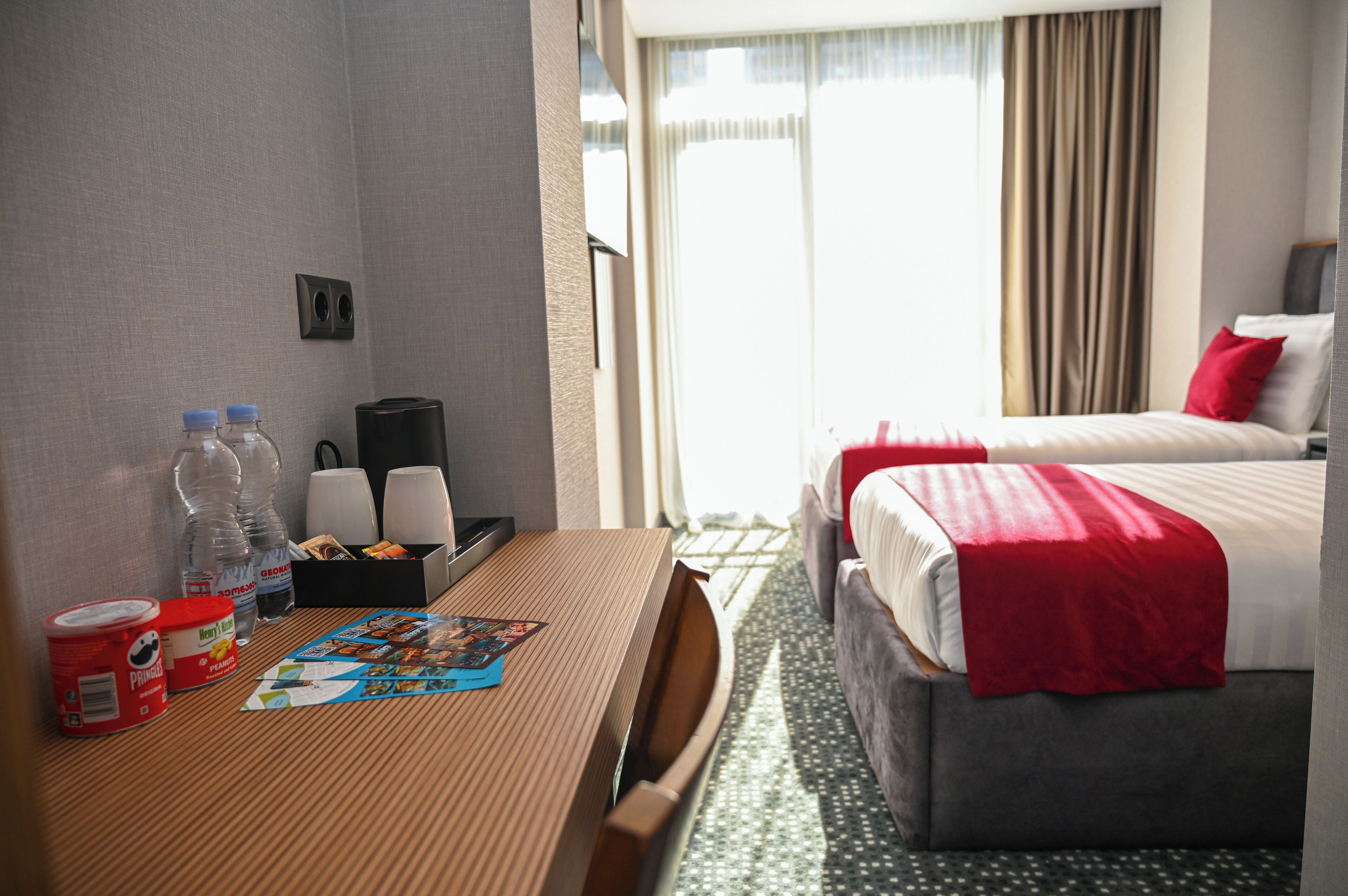 A hotel room with a bed, a table with a magazine, and a window with curtains.