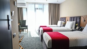 A hotel room with two beds, a desk, a chair, and a large window with curtains. - Landmark Hotel (Batumi)
