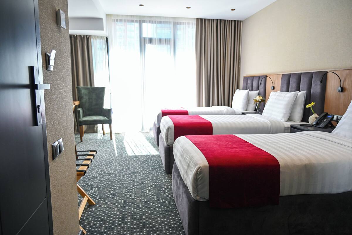 A hotel room with two beds, a desk, a chair, and a large window with curtains.