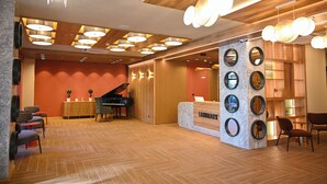 A modern reception area with a wooden reception desk, multiple seating options, and a grand piano. - Landmark Hotel (Batumi)