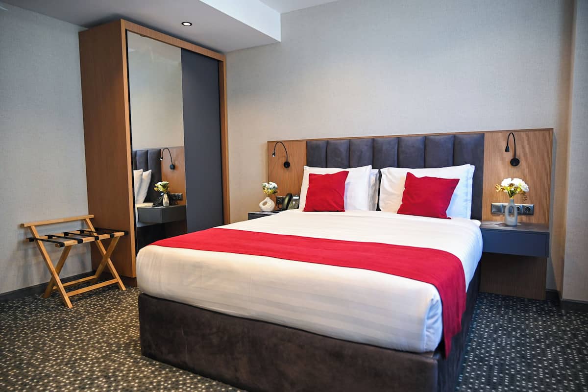 A hotel room with a large bed, a wardrobe, a bedside table with a lamp, and a small table with flowers.