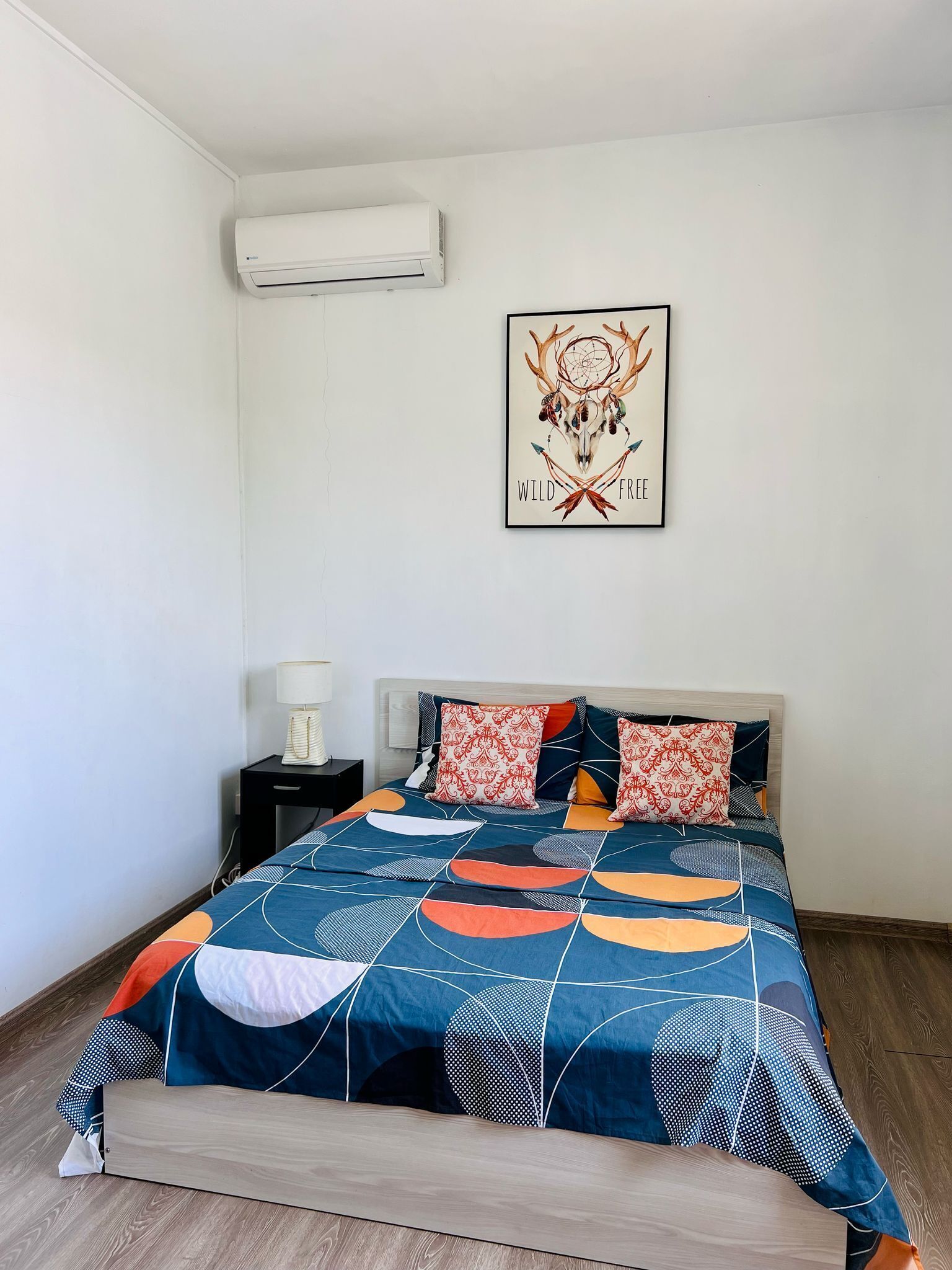 Quarto com cama, mesa de cabeceira, ar-condicionado fixado na parede e uma obra de arte emoldurada.