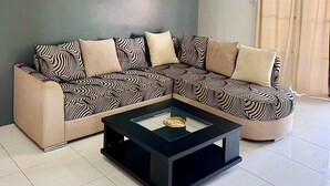Ein modernes Wohnzimmer mit einem Ecksofa, einem Couchtisch mit Glastischplatte und einem Strand-Motiv-Bild an der Wand.