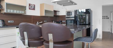 A modern kitchen with two bar stools, a microwave, and a stainless steel refrigerator.