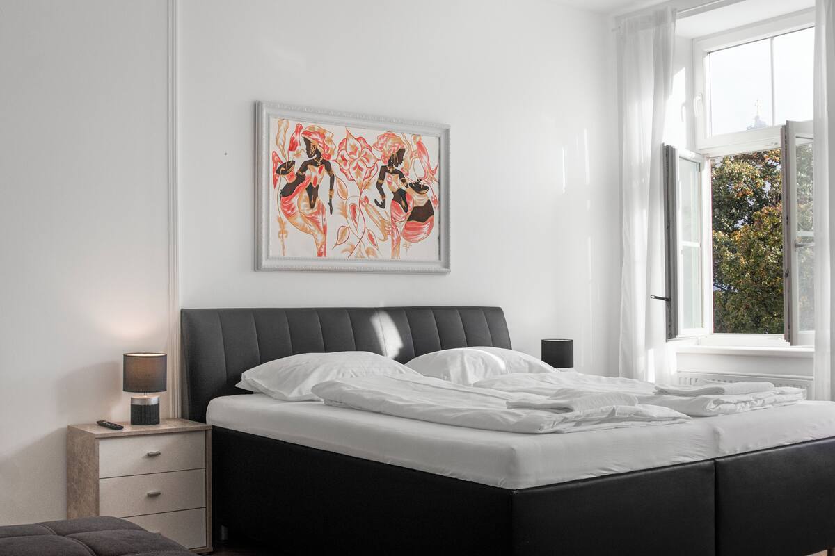 Ein modernes Schlafzimmer mit einem großen Bett, einem Nachttisch mit Lampe und einem gerahmten Kunstwerk an der Wand.