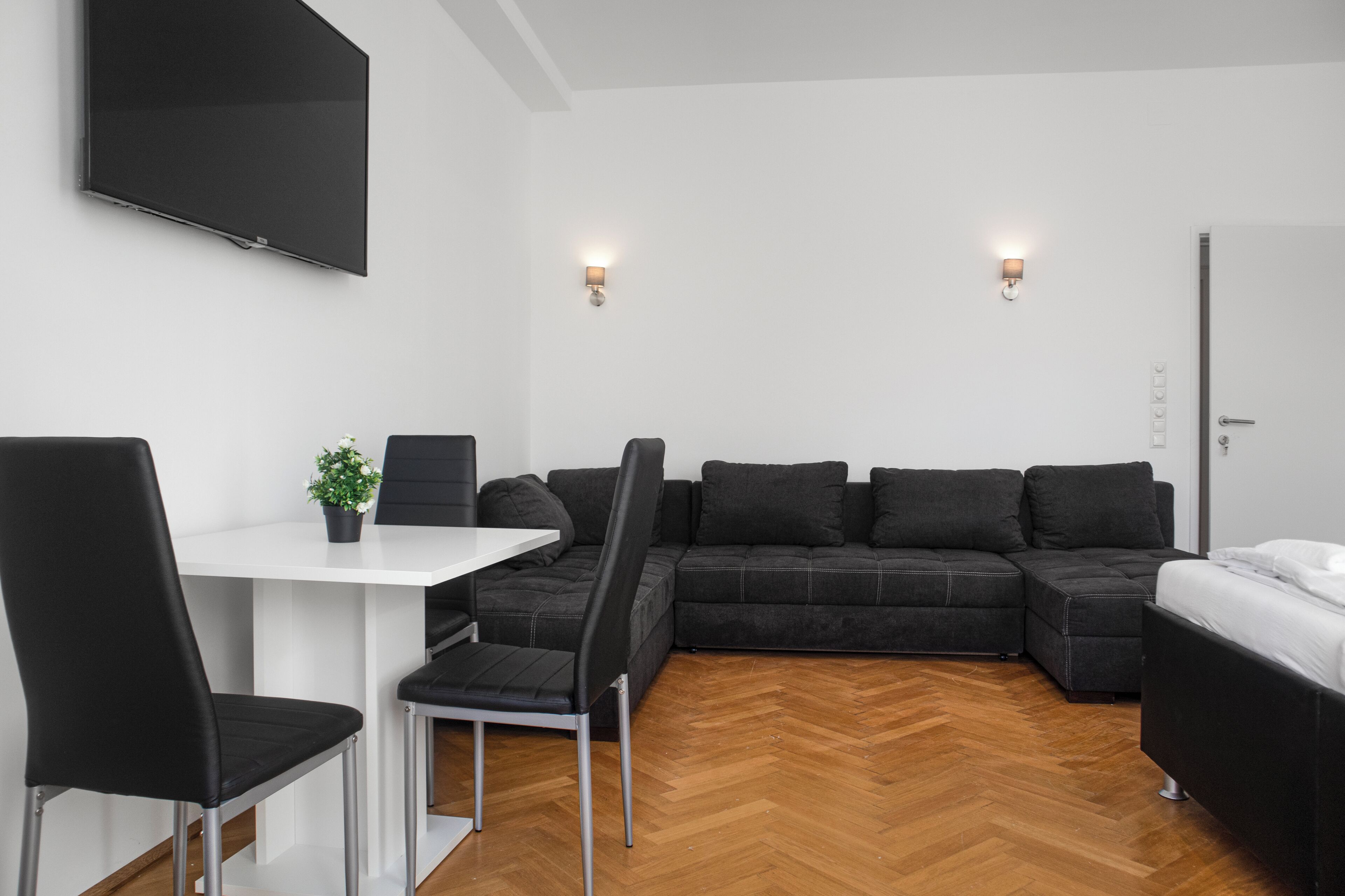 A modern living room with a white table, black chairs, a black sofa, and a TV mounted on the wall.