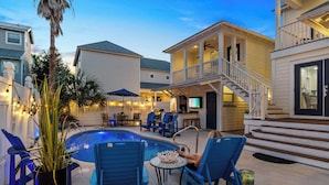 A pool area with blue chairs, a small table, and a staircase leading to a balcony. - Lighthouse Legends-Free Golf Cart-1 Block to Beach (Destin)