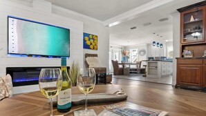 A modern living room with a flat-screen TV, two wine glasses, and a bottle of wine on a wooden table. - Lighthouse Legends-Free Golf Cart-1 Block to Beach (Destin)
