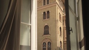 A room with a view of a building with ornate architecture, a chair, and a window with curtains. - Hotel velvet  (Cairo)