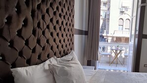 A hotel room with a tufted headboard, a large bed with white linens, and a view of the city through an open door. - Hotel velvet  (Cairo)