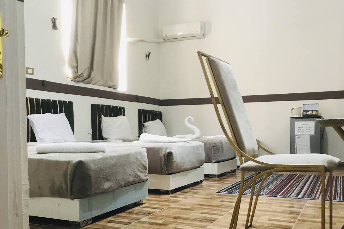 A hotel room with two beds, a chair, a desk, and a water meter.