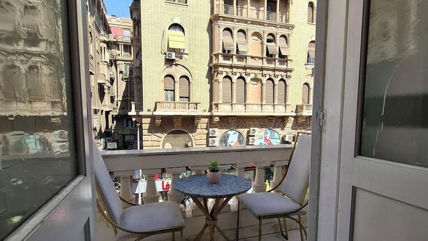 A balcony with two chairs and a small table, overlooking a historic building with ornate architecture. - Hotel velvet  (Cairo)