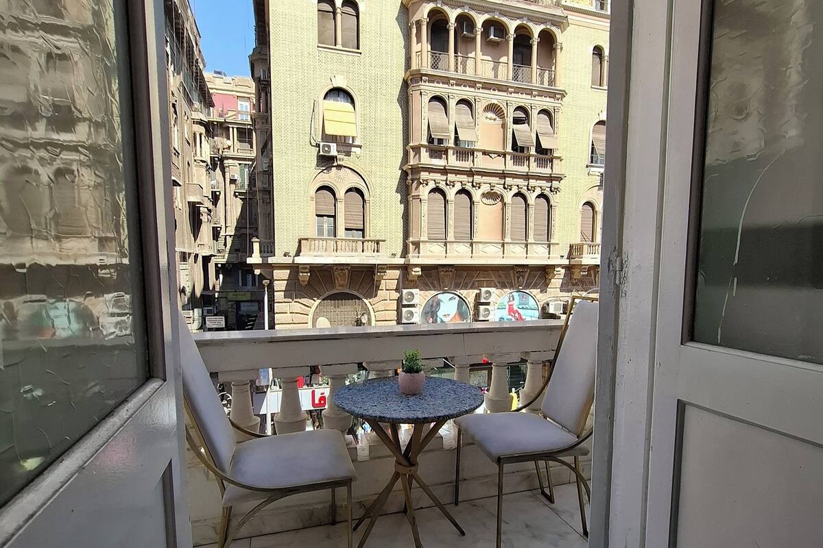 A balcony with two chairs and a small table, overlooking a historic building with ornate architecture.
