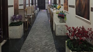 A hallway with a marble floor, flanked by chairs and tables, leading to a door. - Hotel velvet  (Cairo)