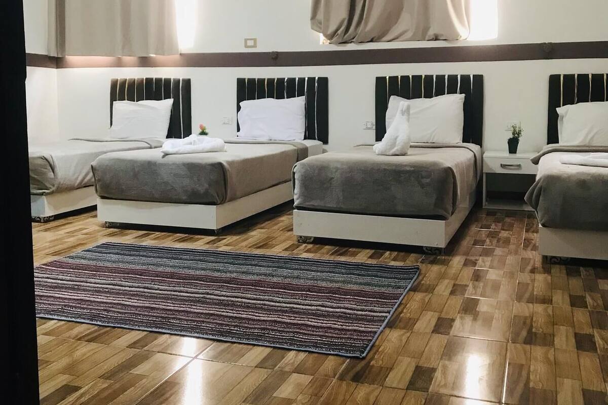 A hotel room with three beds, a wooden floor, and a striped rug.