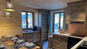 A modern kitchen with wooden cabinetry, a dining area with a wooden table set for a meal, and large windows providing natural light.