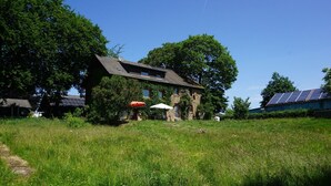 Une maison avec une façade en pierre, une cour gazonnée et des panneaux solaires sur le toit.