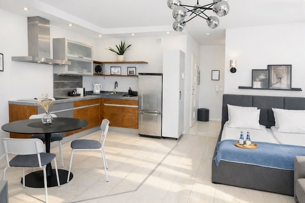 A modern kitchen with a dining area, a grey sofa, and a ceiling light fixture.