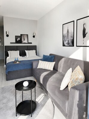 Une chambre à coucher moderne avec un lit, un canapé gris, une petite table ronde et des œuvres d’art accrochées aux murs.