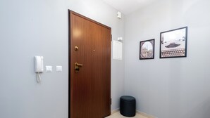 Un couloir avec une porte en bois, un téléphone blanc, une petite poubelle et deux tableaux encadrés accrochés au mur.