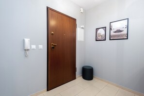 Ein Flur mit einer Holztür, einem weißen Telefon, einer kleinen Mülltonne und zwei gerahmten Bildern an der Wand.