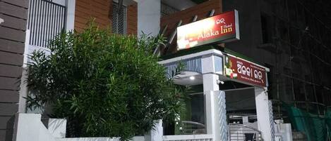 A hotel named Alaka Inn with a signboard, a gated entrance, and a small garden area.