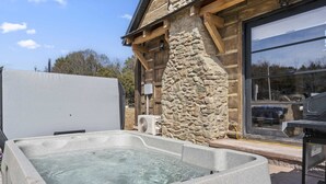 A stone exterior wall, a wooden deck, and a hot tub. - Elk Lodge – Cabin for 4! (Branson)