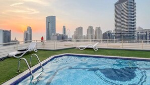 Una piscina sul tetto con poltrone a sdraio e uno skyline urbano sullo sfondo.
