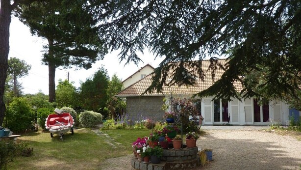 A house with a gravel driveway, surrounded by a garden with potted plants and a red boat.