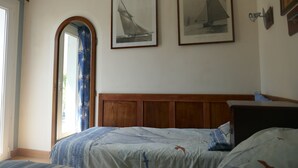 A bedroom with a wooden headboard, a bed with a patterned bedspread, and two framed pictures of sailboats on the wall.