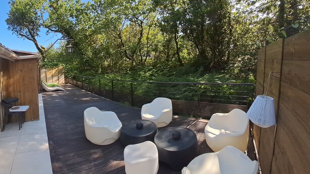 Un espace extérieur aménagé avec des chaises et des tables blanches, entouré d’arbres et d’une clôture en bois.