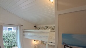Une chambre avec un lit superposé, une fenêtre, une échelle et une petite étagère.