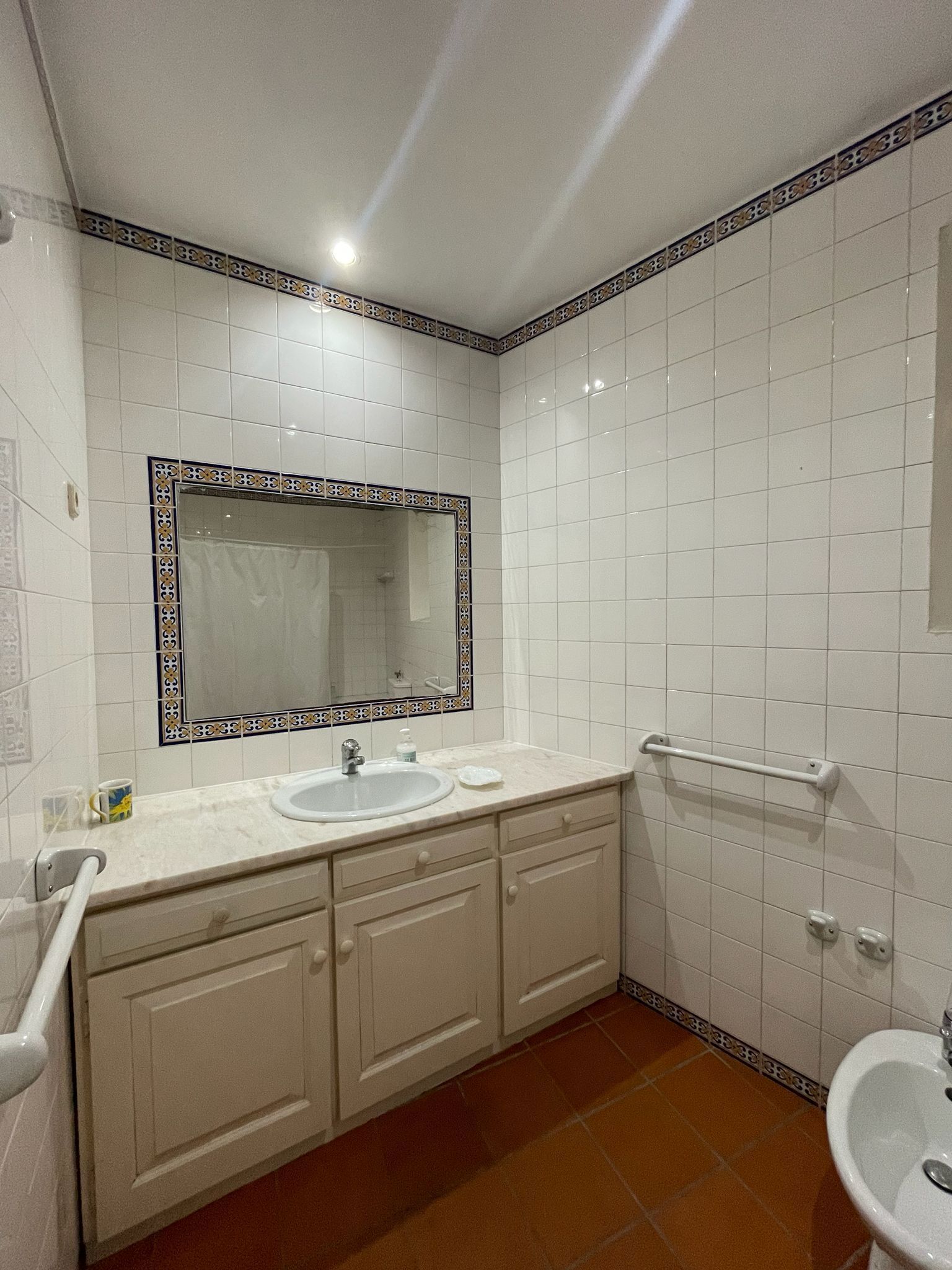 A bathroom with white tiled walls, a large mirror with decorative border, a sink, a toilet, and a bidet.