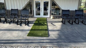 A covered outdoor seating area with chairs and a central artificial grass feature, under a white roof with a door and windows.