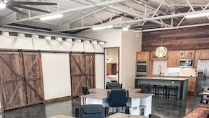 A modern office space with a large conference table, black office chairs, and a kitchen area with wooden cabinets and stainless steel appliances.