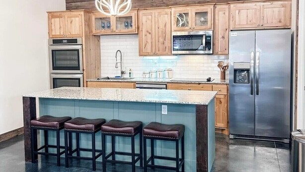 A modern kitchen with wooden cabinets, stainless steel appliances, and a central island with bar stools.