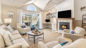A spacious living room with a fireplace, comfortable seating, a television, and a large window. - Sunset Landing: Waterfront Luxury Condo with High End Finishes Throughout (Douglas)