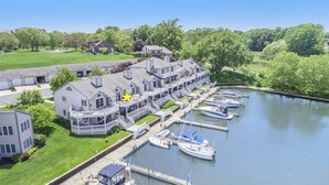 A waterfront hotel with multiple balconies, a marina with boats, and a well-maintained lawn. - Sunset Landing: Waterfront Luxury Condo with High End Finishes Throughout (Douglas)
