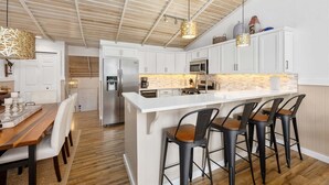 A modern kitchen with white cabinets, a stainless steel refrigerator, a central island with bar stools, and pendant lighting. - Sunset Landing: Waterfront Luxury Condo with High End Finishes Throughout (Douglas)
