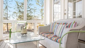 Une véranda avec un canapé en osier, une table en verre et un fauteuil.