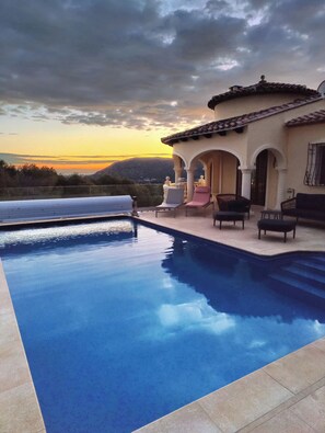 A swimming pool with a view of a sunset and mountains in the background.