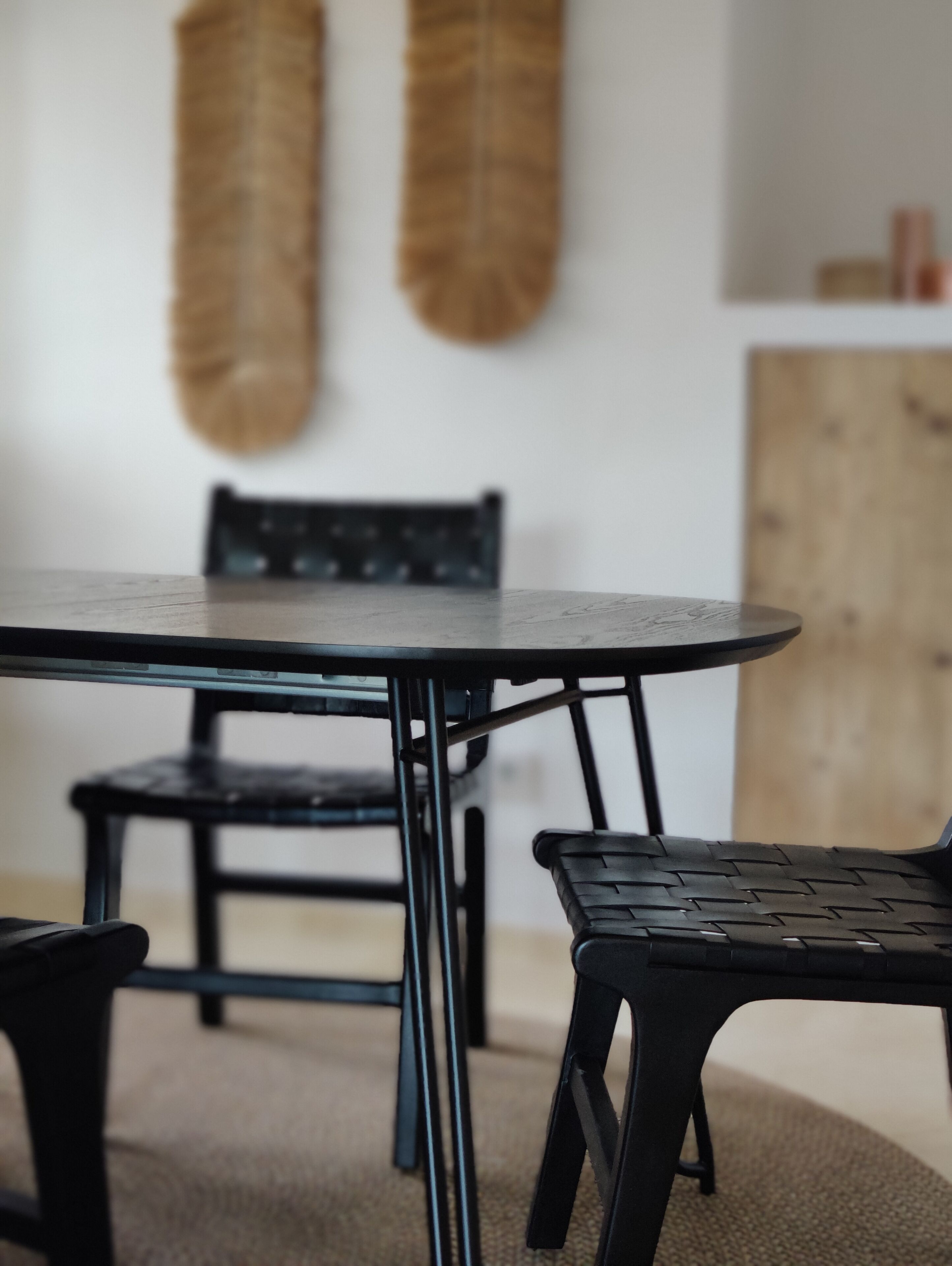 A round table with a black metal frame, two black chairs with woven seats, and a wooden cabinet in the background.