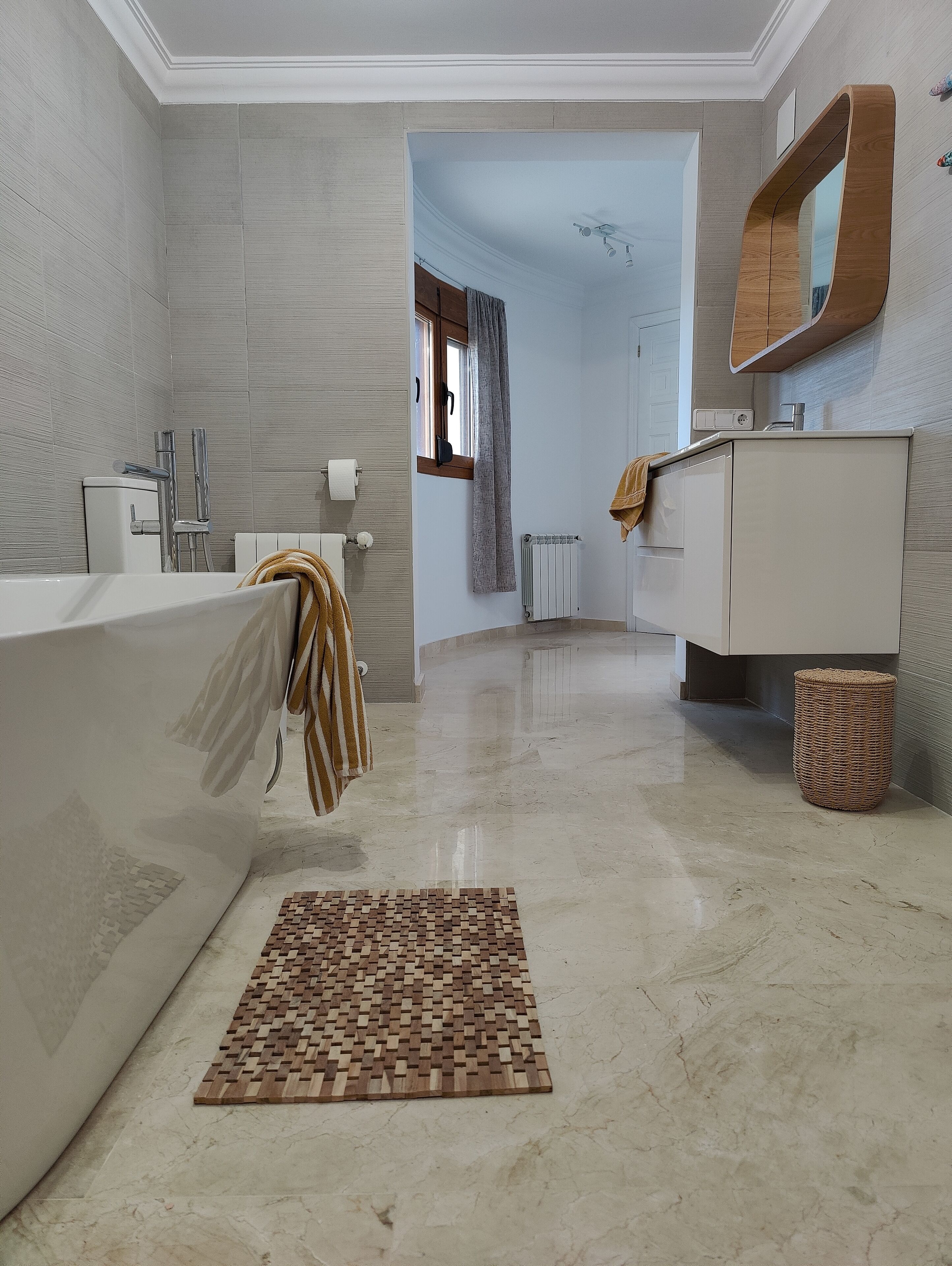 Un baño moderno con una bañera grande, un felpudo de madera y un tocador blanco.