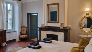 Un dormitorio con cama, cómoda, silla, chimenea y espejo.