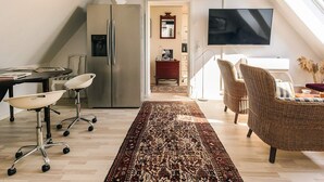 Eine moderne Küche mit integriertem Kühlschrank, einem Essbereich mit rundem Tisch und Stühlen, einem großen Teppich und einem an der Wand befestigten Fernseher.