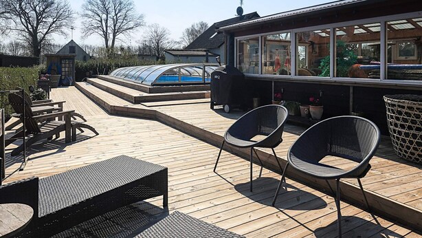 Eine Holzterrasse mit Sitzgelegenheiten im Freien, einem Grill und einem Pool mit Glasveranda.