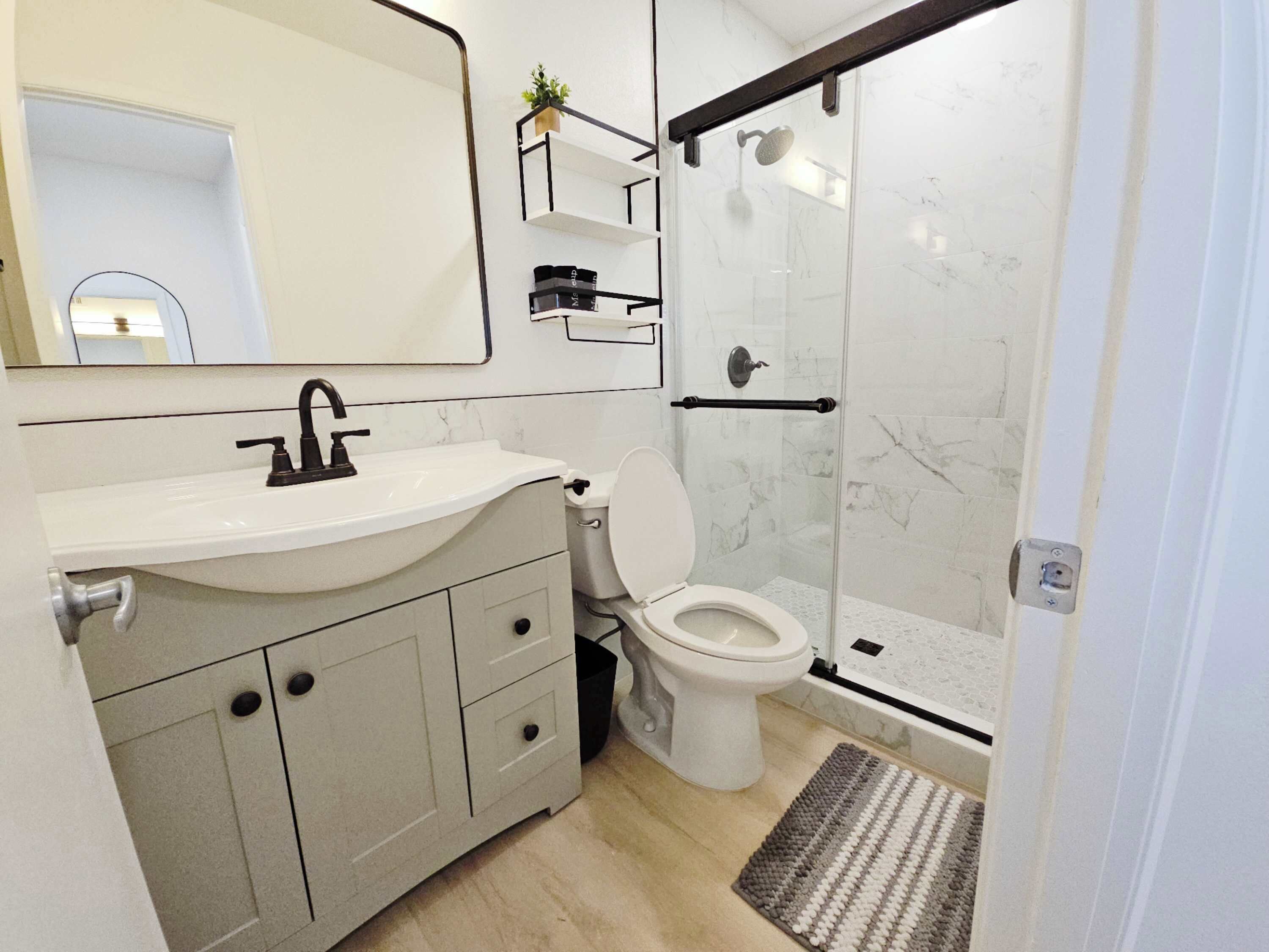 Ein modernes Badezimmer mit einem weißen Waschbecken, einer Toilette, einer Duschkabine aus Glas und einer kleinen Ablage für Toilettenartikel.
