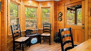 A wooden cabin with large windows, two chairs, a table, and a bear decoration. - New! Riverfront Retreat - Sleeps 12, Ellijay (Ellijay)