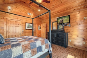 Ein Schlafzimmer einer Holzhütte mit einem Bett, einem Schminktisch, einem Fernseher und einem Deckenventilator.