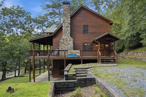 Une cabane en rondins avec une cheminée en pierre, une véranda et un escalier en pierre menant à l’entrée.